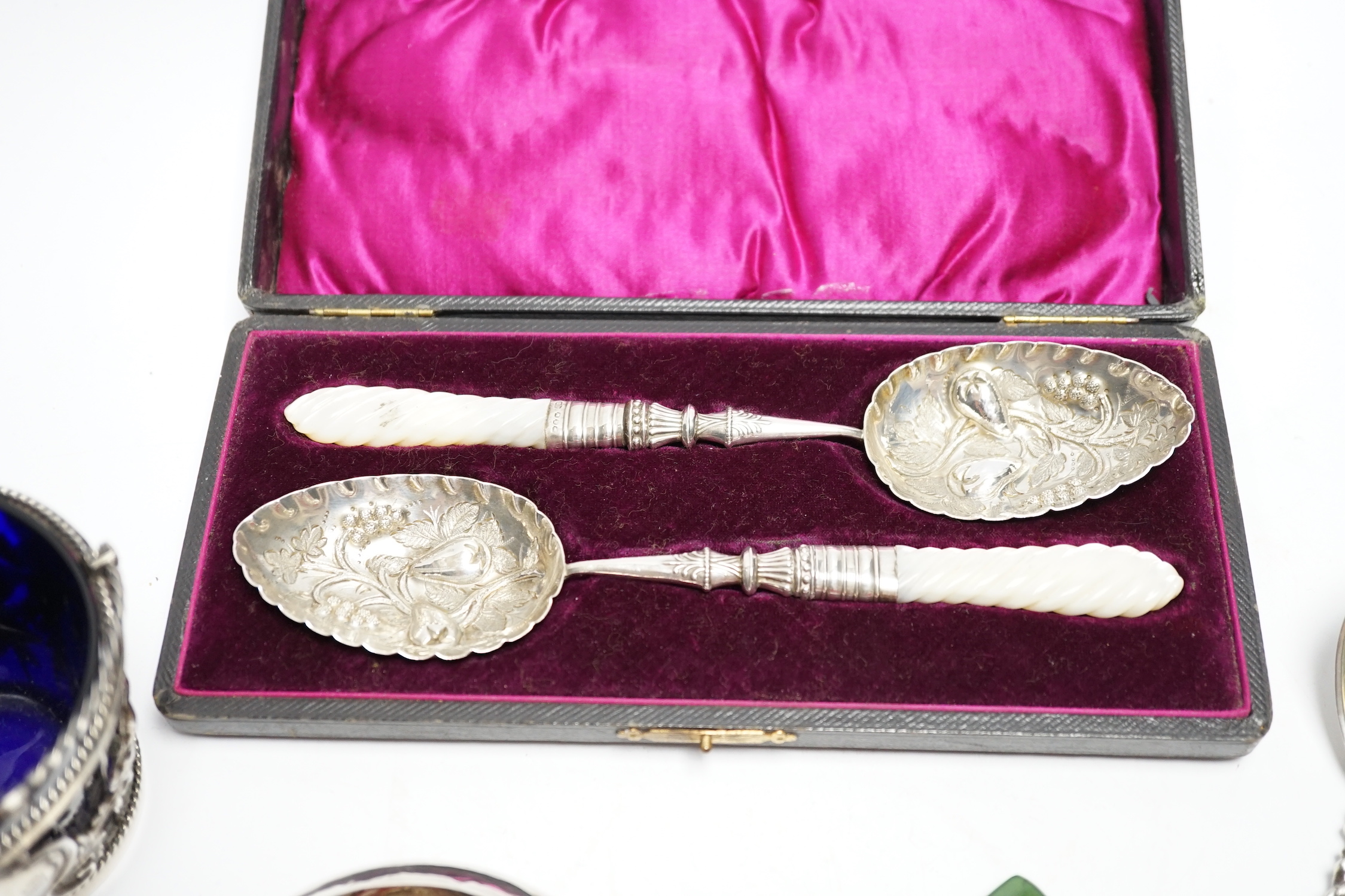 A cased pair of late Victorian mother of pearl handled silver 'berry' spoons, by A.J. Bailey, Birmingham, 1896, a continental white metal spoon with figural terminal, a pierced white metal sugar basket, with blue glass l